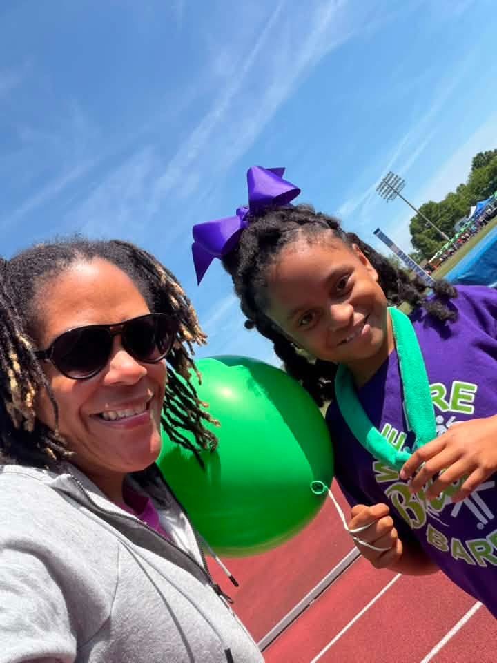 An adult and a child posing outdoors beside a green balloon